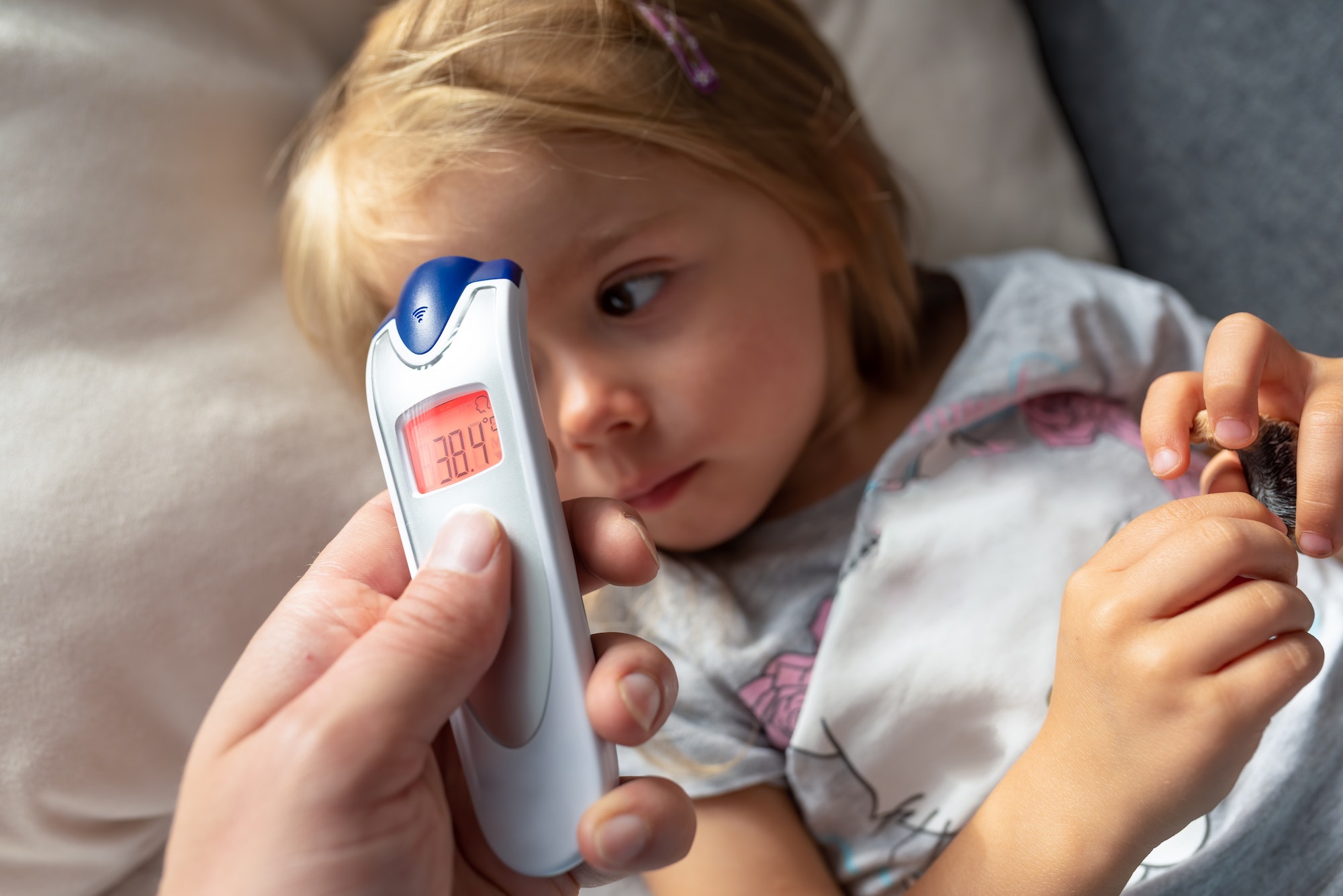 Parent takes temperature for her child with infrared thermometer at home, high fever